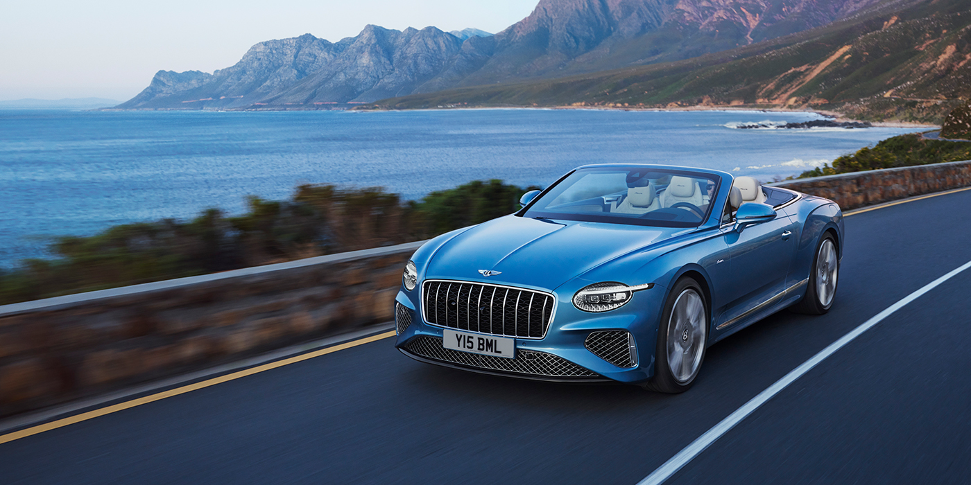 Bentley Padova New Bentley Continental GTC Azure convertible in Light Windsor blue paint with 22 inch Azure wheels and chrome grill, driving dynamically by the sea