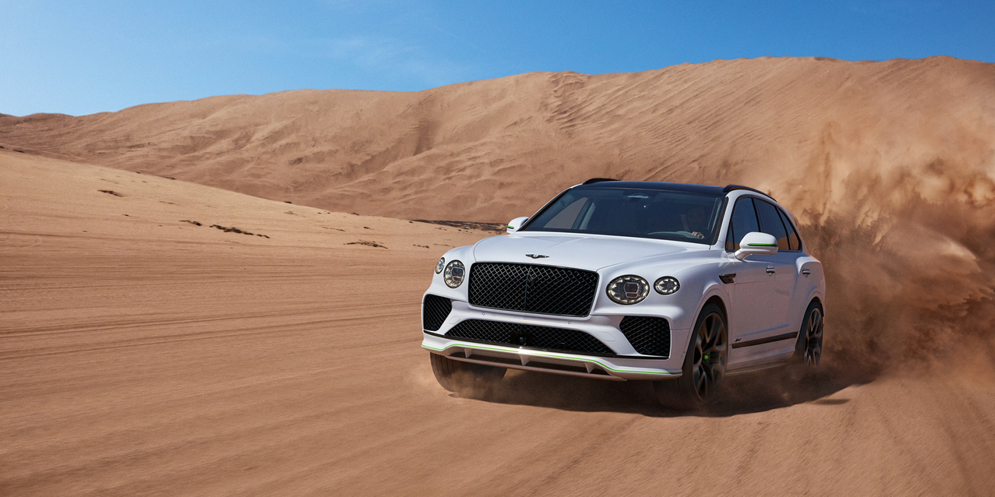 Bentley Padova Bentley Bentayga Speed SUV front three quarter in Snow Quarts Pearlescent by Mulliner white paint driving dynamically through the desert