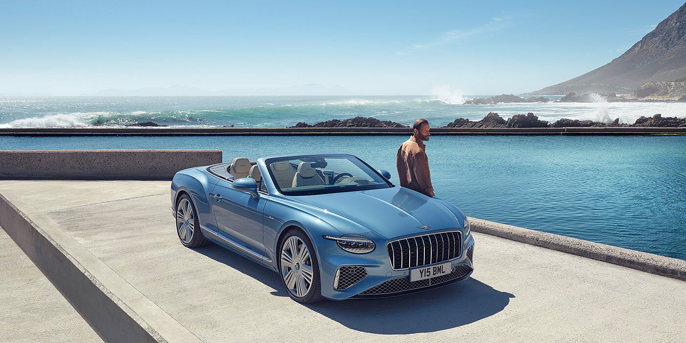 Bentley Padova New Bentley Continental GTC Azure convertible front view in Light Windsor blue paint with 22 inch ten spoke wheels parked by the sea in the sunshine