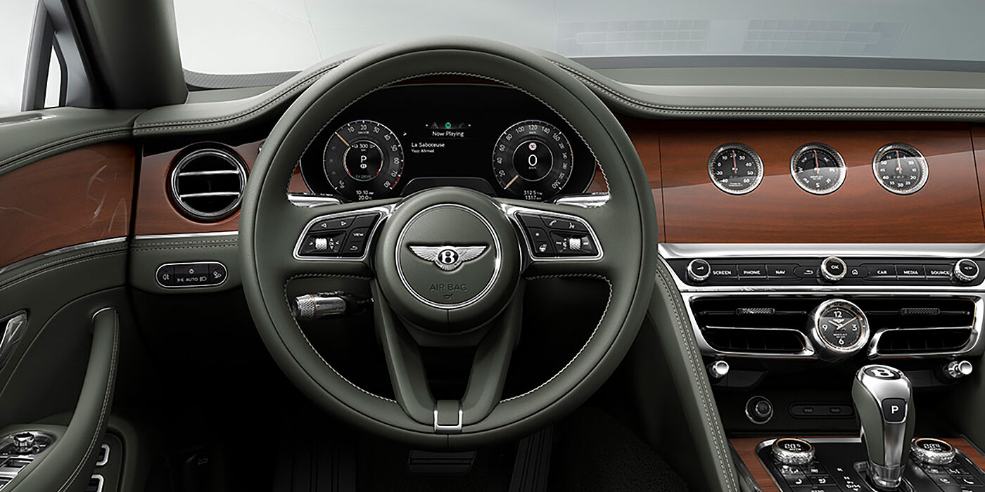 Bentley Padova New Bentley Flying Spur sedan front cabin in Cumbrian Green hide and Crown Cut walnut veneer showing steering wheel and Rotating Display with three clocks on face