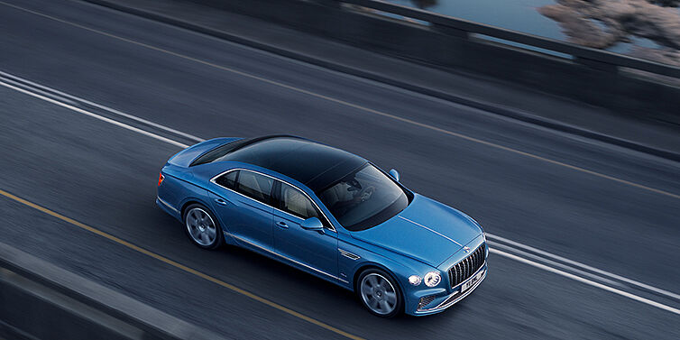 Bentley Padova New Bentley Flying Spur Azure sedan in Light windsor blue paint by Mulliner, with 22 inch Azure wheels seen from overhead driving dynamically on a country road