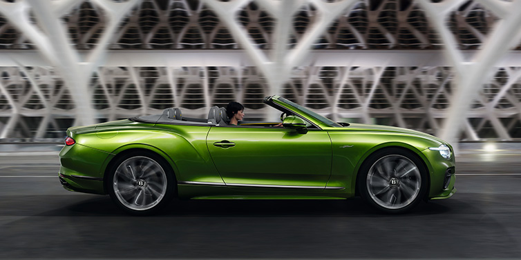 Bentley Padova Bentley Continental GTC Speed convertible side profile in Tourmaline Green paint driving dynamically on a bridge at night