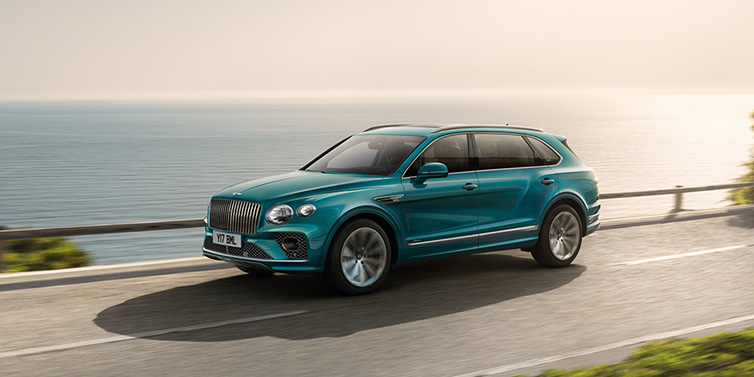 Bentley Padova Bentley Bentayga Extended Wheelbase Azure SUV in Topaz blue paint driving dynamically by the ocean