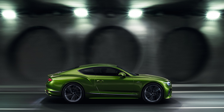 Bentley Padova Bentley Continental GT Speed coupe profile in Tourmaline Green driving dynamically past a concrete wall at night