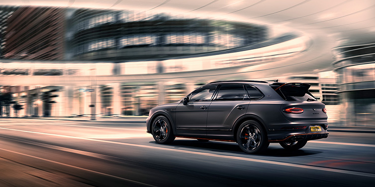 Bentley Padova Bentley Bentayga S Black Edition SUV rear three quarter in Anthracite Satin paint driving dynamically through a city at night