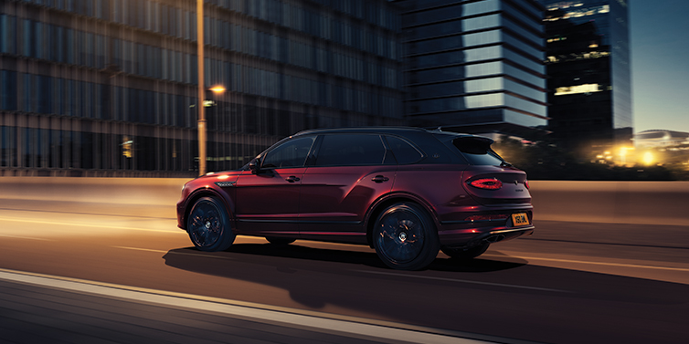 Bentley Padova Bentley Bentayga Extended Wheelbase Mulliner SUV in Cricket Ball red paint driving dynamically in city at night