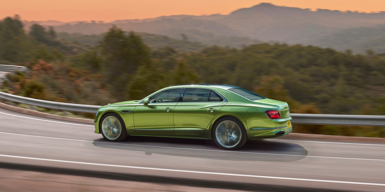 Bentley Padova Bentley Flying Spur Speed sedan side profile in Tourmaline Green paint driving dynamically on a mountain road at sunset