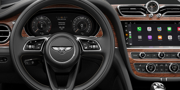 Bentley Padova Bentley Bentayga SUV front interior detail of steering wheel and driver screens surrounded by Beluga black hide and Crown Cut Walnut veneer