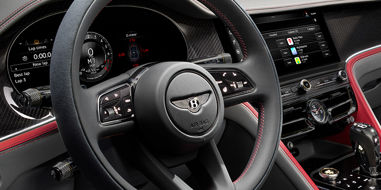 Bentley Padova Bentley Flying Spur Speed sedan front interior detail showing steering wheel and driver screens surrounded with Hotspur red and Gravity Grey hides